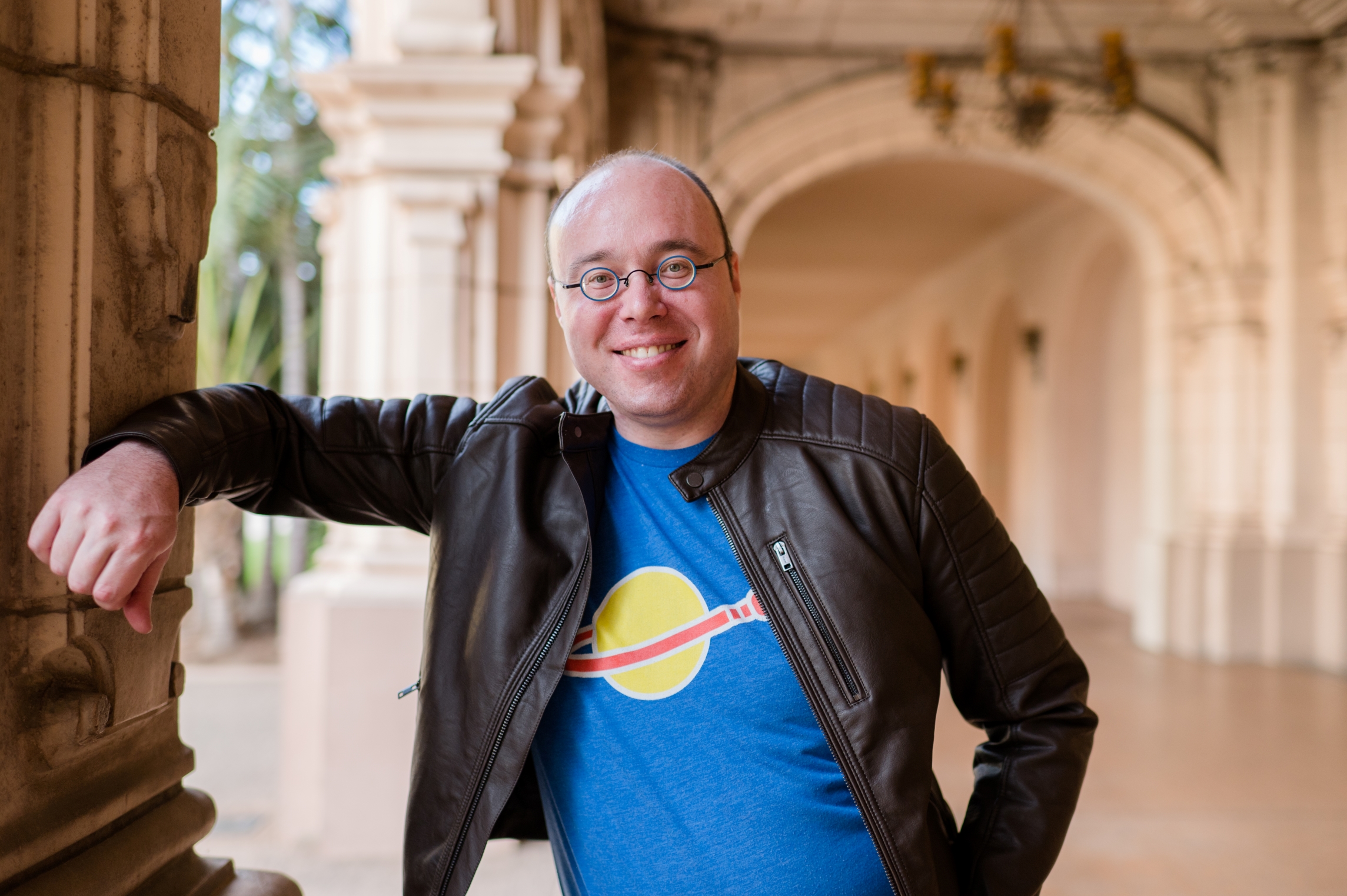 Photo of Eric Marc-Aurele. Wearing a blue shirt with Lego Space logo under a faux leather motorcycle jacket.